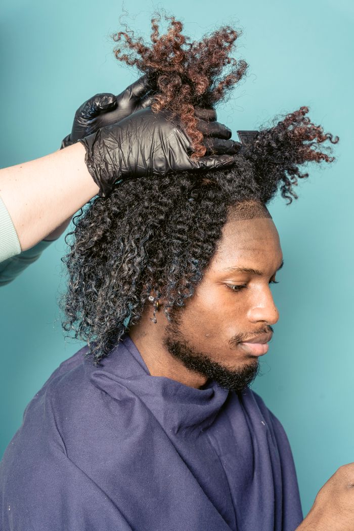 Side view of bearded African American male with dark dyed curly hair sitting in barbershop and looking down